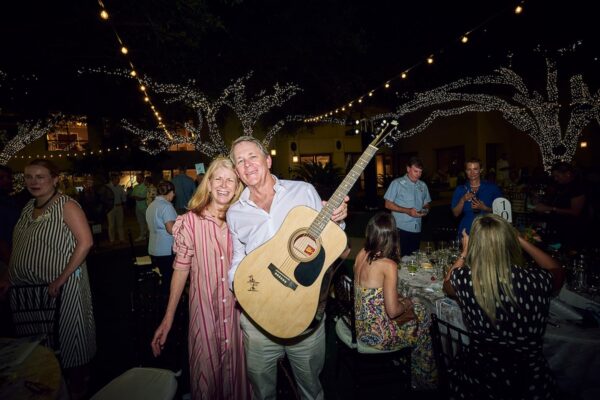 auction winner posing with a signed acoustic guitar under string lights at night
