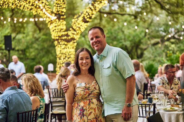 couple posing in front of a tree wrapped in lights at the outdoor dinner