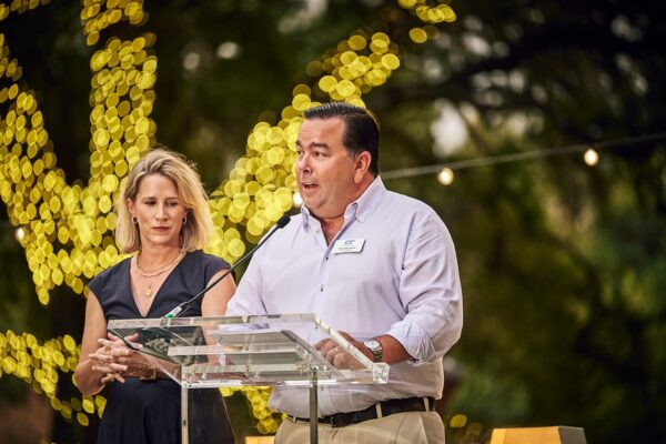 two speakers addressing guests from a clear podium beneath lit trees