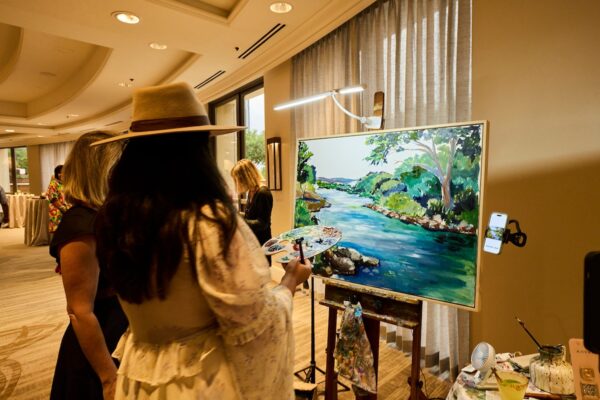 artist in a wide-brimmed hat painting a Colorado River landscape live on an easel during the event