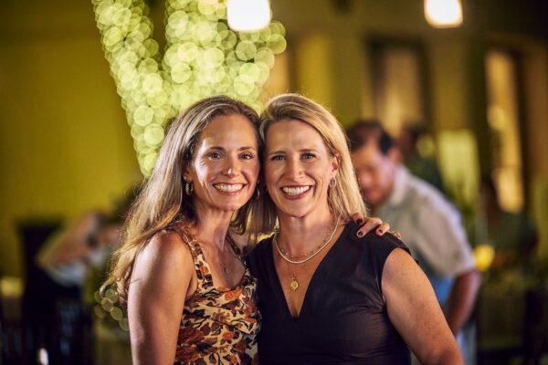 two guests smiling cheek to cheek in front of a light-wrapped tree