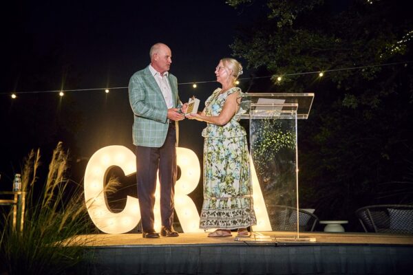 Adrienne Longenecker presenting an award to Phil Wilson at the podium beside glowing CRA letters on the outdoor stage