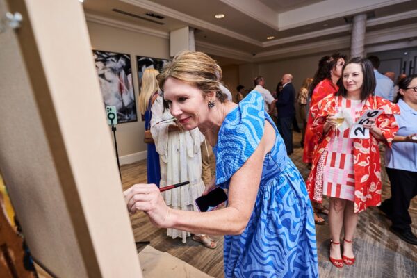 guest in a blue dress adding brushstrokes to a community painting during the reception